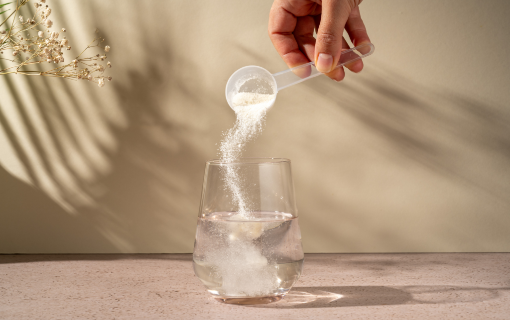 A handing pouring a collagen peptide powder into a glass of water