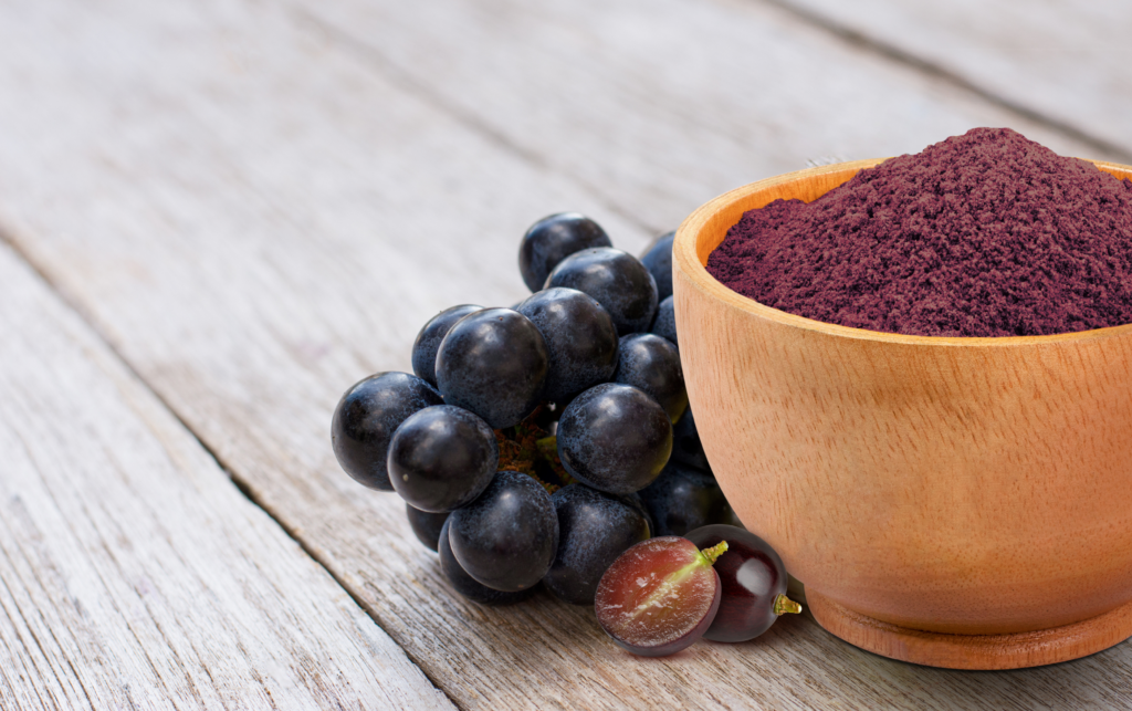 A purple resveratrol powder sits in a bowl next to grapes